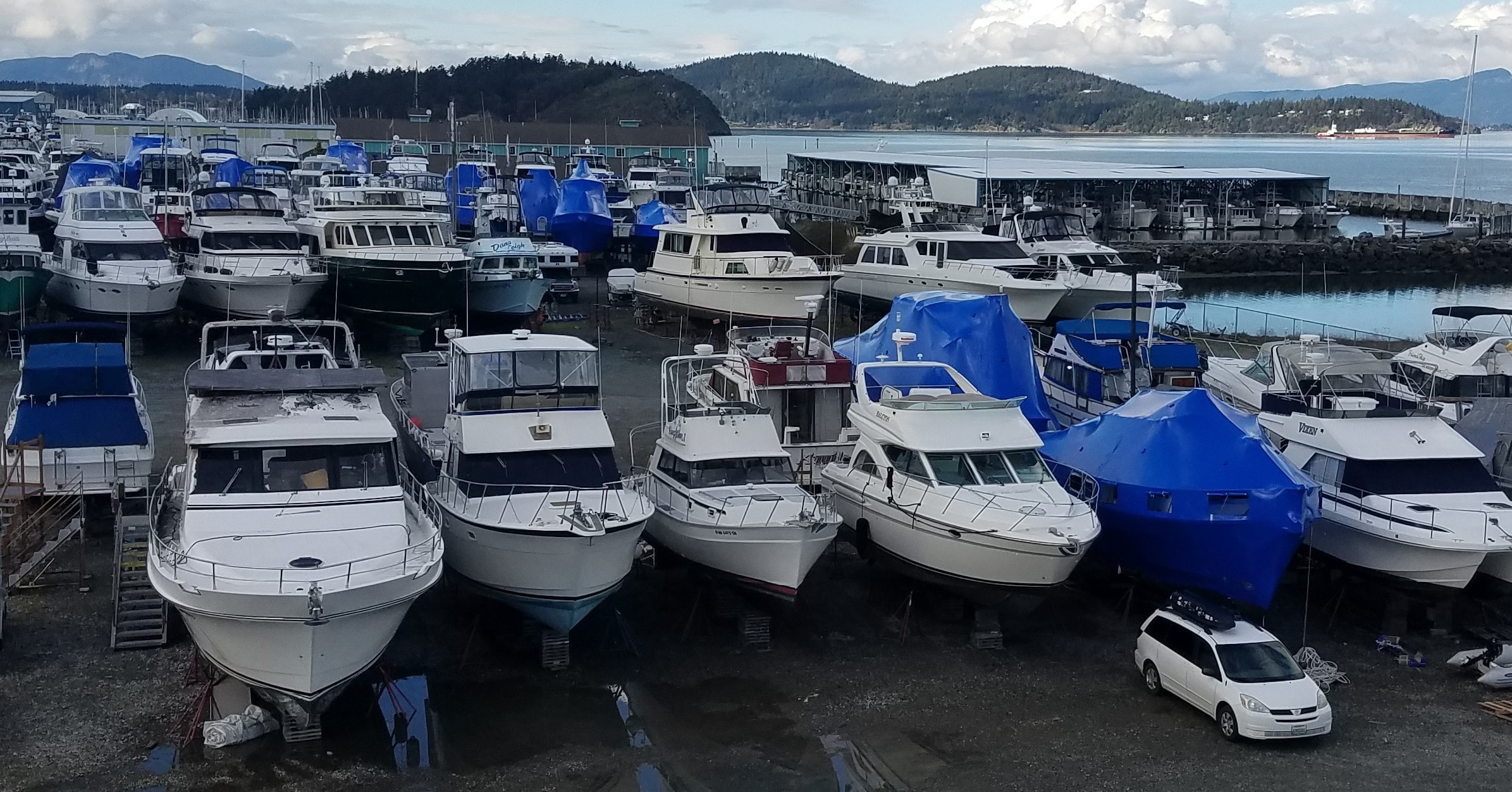 Aerial overview of North Harbor Diesel boatyard with dozens of vessels in dry storage, Anacortes waterfront and Cascade Mountains in background