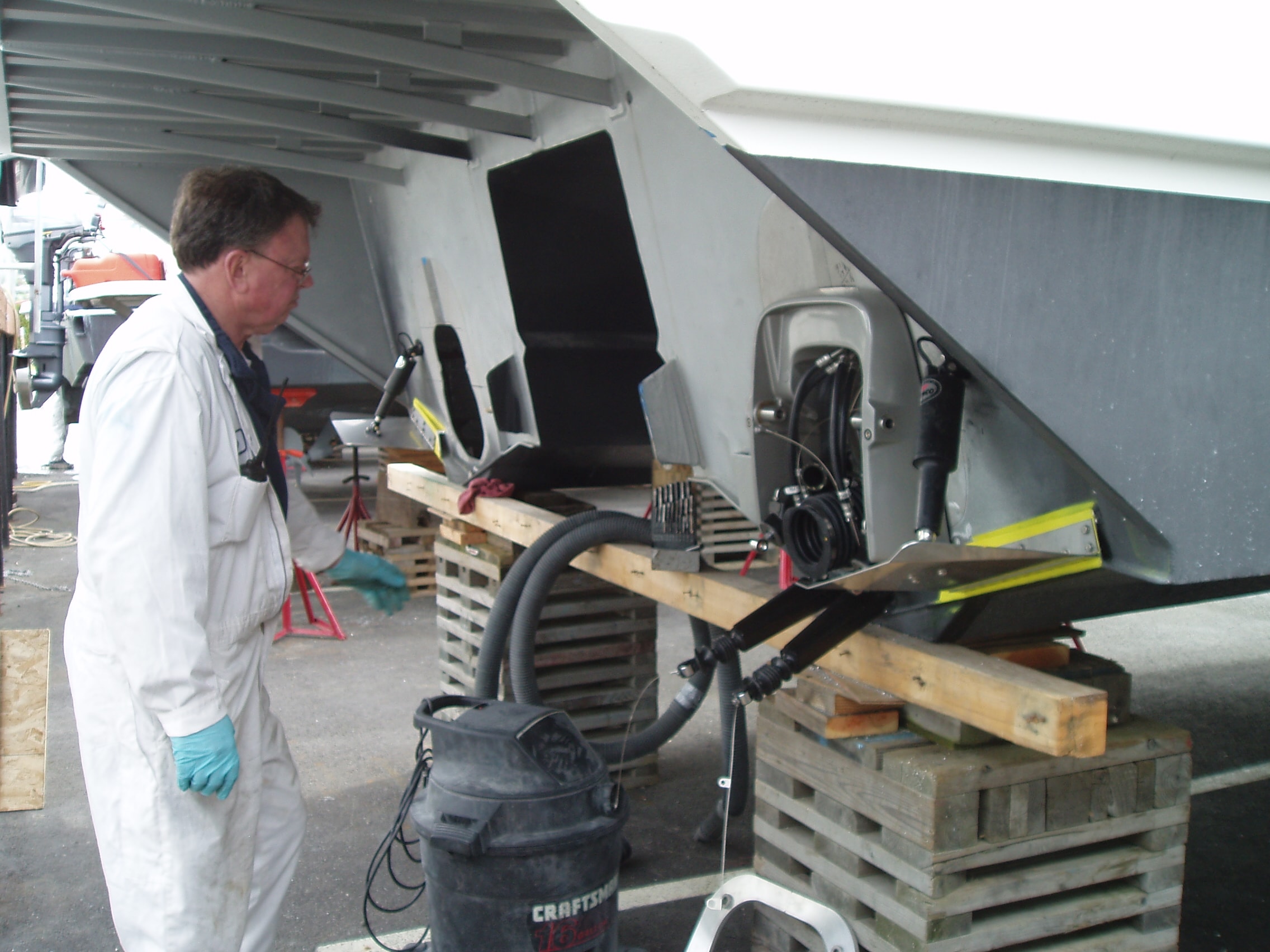 NHD technician in white coveralls and blue gloves inspecting Maxcat sterndrive engine components with shop-vac during service