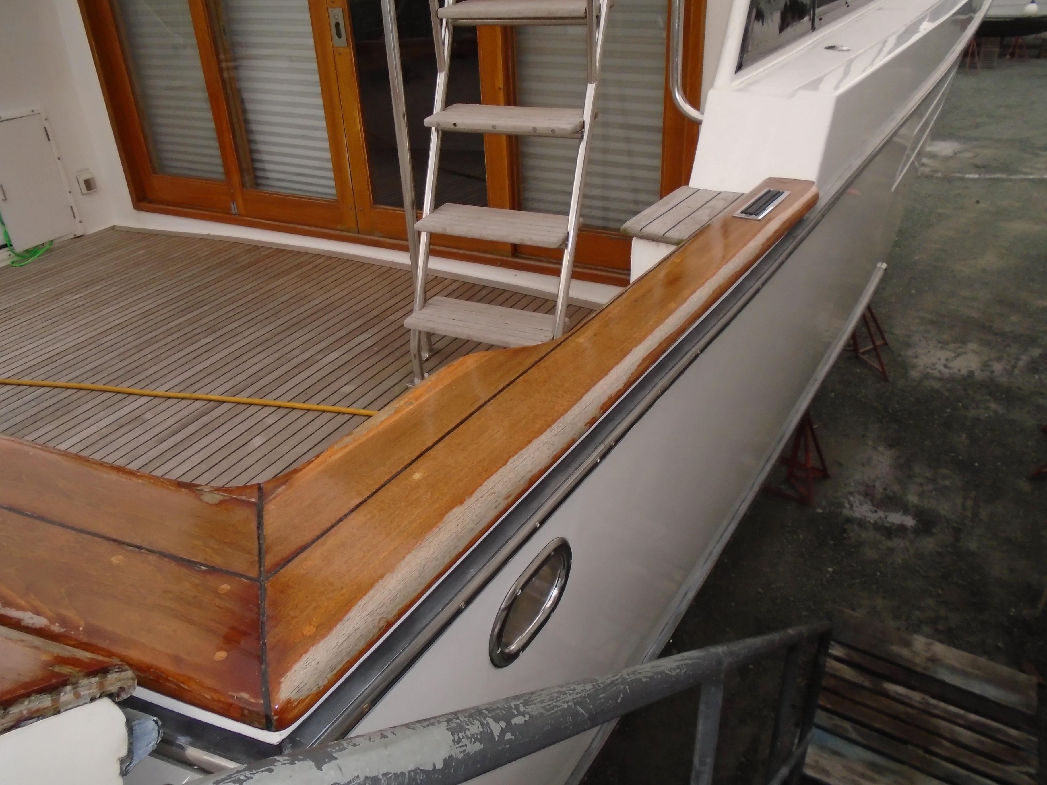 Freshly varnished teak cap rail and aft deck on yacht in NHD boatyard — before refinishing